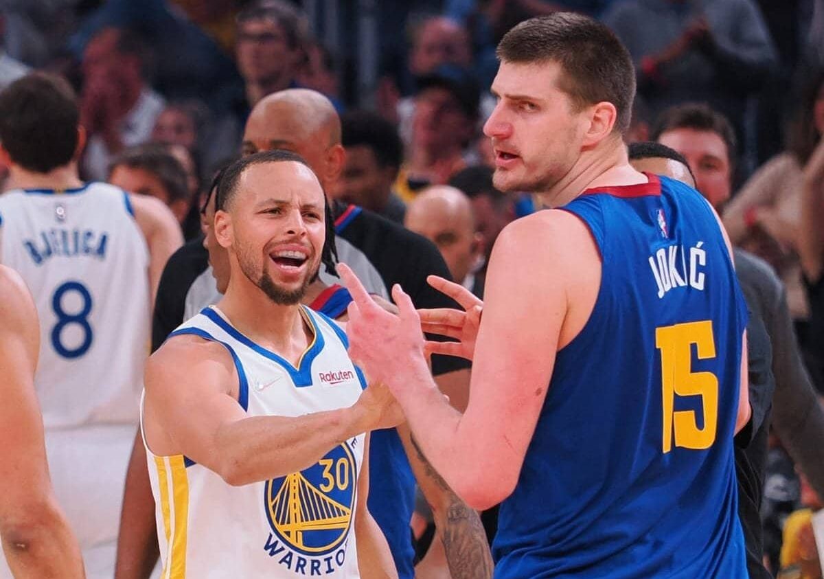 STEPHEN CURRY DE LOS WARRIORS A LA IZQUIERDA Y NIKOLA JOKIC DE LOS NUGGETS, DISCUTEN EN UN PARTIDO