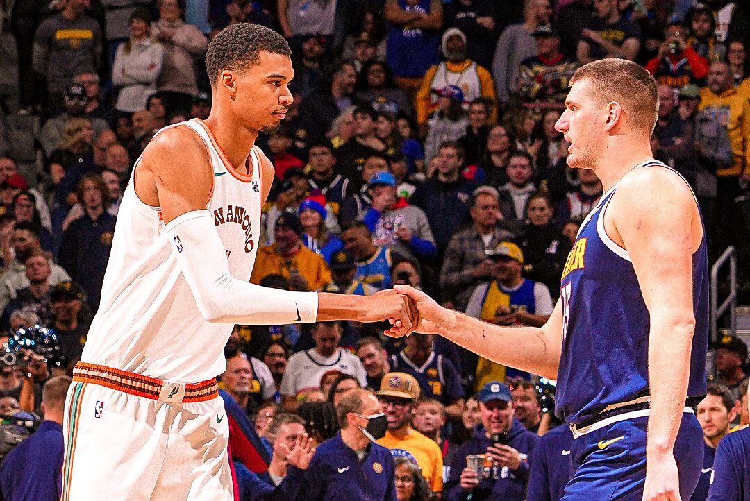 WEMBANYAMA DE LOS SPURS A LA IZQUIERDA, SALUDANDO A JOKIC DE LOS NUGGETS A LA DERECHA